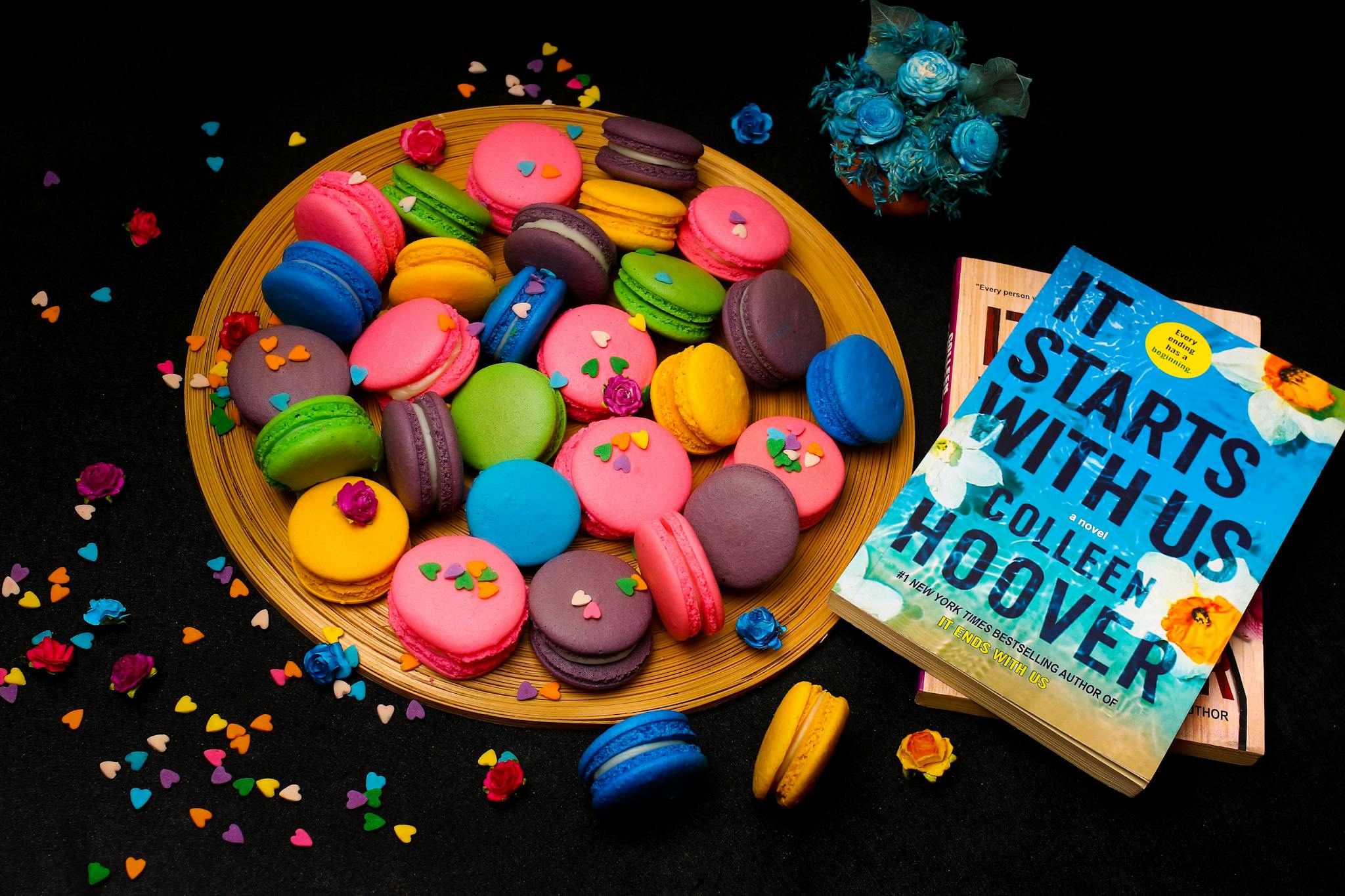 A vibrant display of assorted macarons next to a novel and flowers.