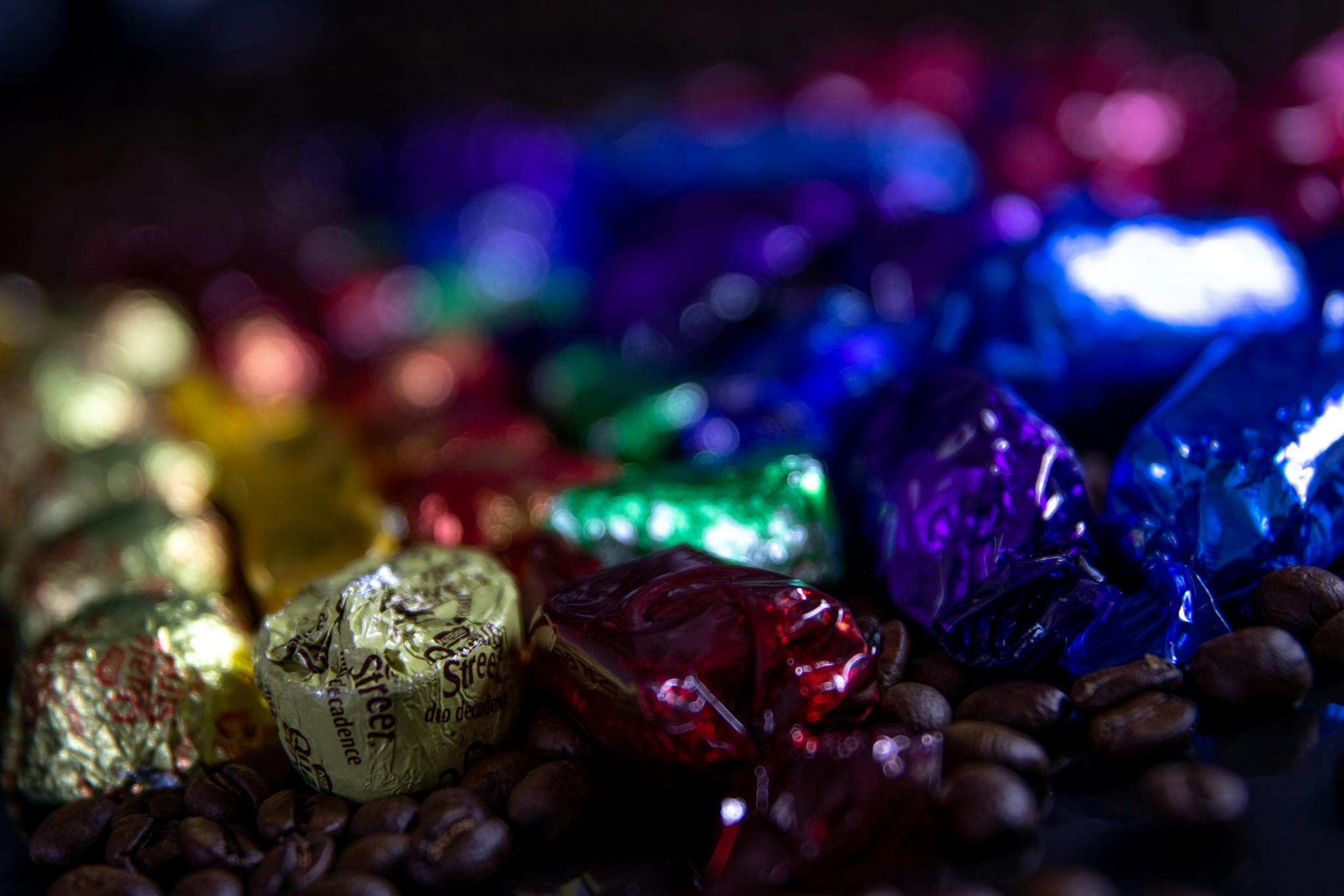 Close-up of vibrant wrapped candies scattered over coffee beans with a blurred background.
