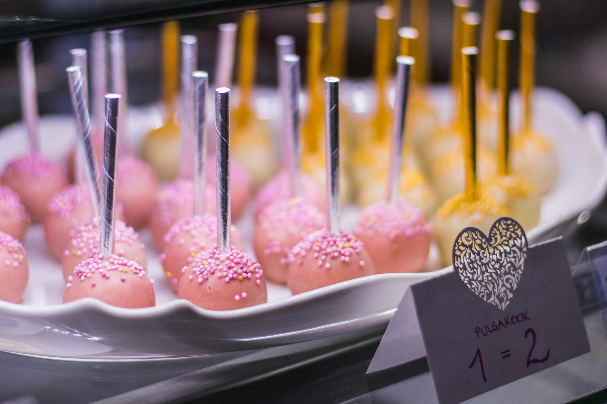 Vibrant pink and yellow cake pops on a white plate, perfect for parties and celebrations.